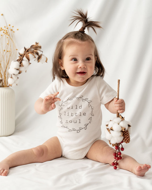 Short sleeve unisex baby bodysuit, featuring a hand-draw spring wreath and a slogan “wild little soul” at the front.  Envelope neckline design and snap buttons for effortless dressing and nappy changing.