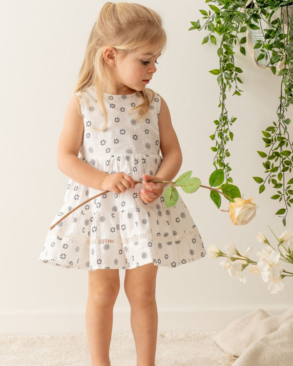 Little girl dressing Organicline Sweetheart dress, softly made from organic cotton in woven , featuring abstract chamomile flower pattern on natural white. Unique lace eyelet embroidered on the  ruffled dress hemline.