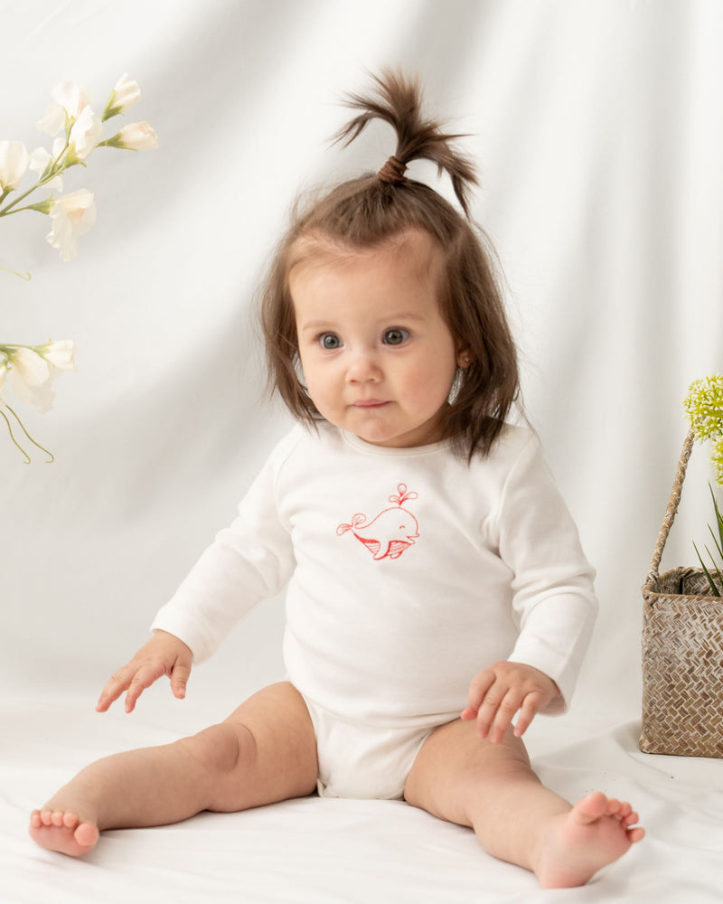 Baby girl wearing long sleeve white color unisex baby bodysuit, featuring a hand-draw cute little dolphin embroidered at the front. Snap buttons on the left shoulder and bottom for effortless dressing and nappy changing.