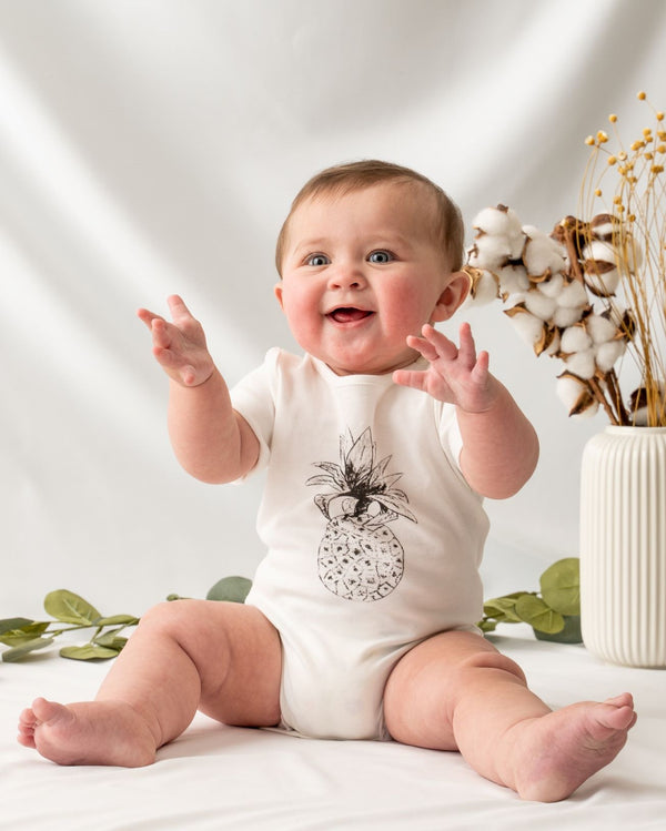 Short sleeve undyed natural white unisex baby bodysuit, featuring a hand-draw pineapple at the front and snap buttons on the left shoulder and the bottom for easy dressing and nappy changing.